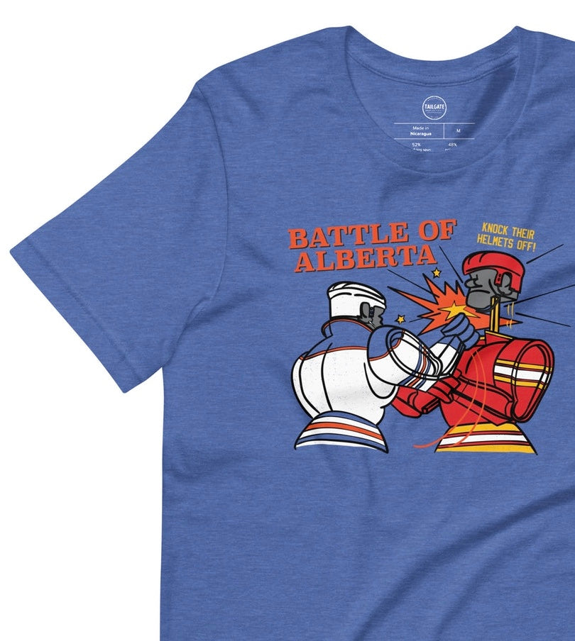 Image of heather royal blue t-shirt with design of "Battle of Alberta" with rock'em, sock'em style hockey players fighting located on centre chest. Players in the design are completed in NHL Calgary Flames and Edmonton Oilers colours. This design is exclusive to Tailgate Mercantile and available only online.
