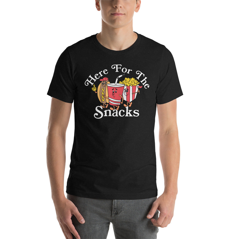 Image of young man wearing heather black tee with design of "Here For The Snacks" with cartoon hot dog, soda pop and popcorn located on centre chest. This design is exclusive to Tailgate Mercantile and available only online.