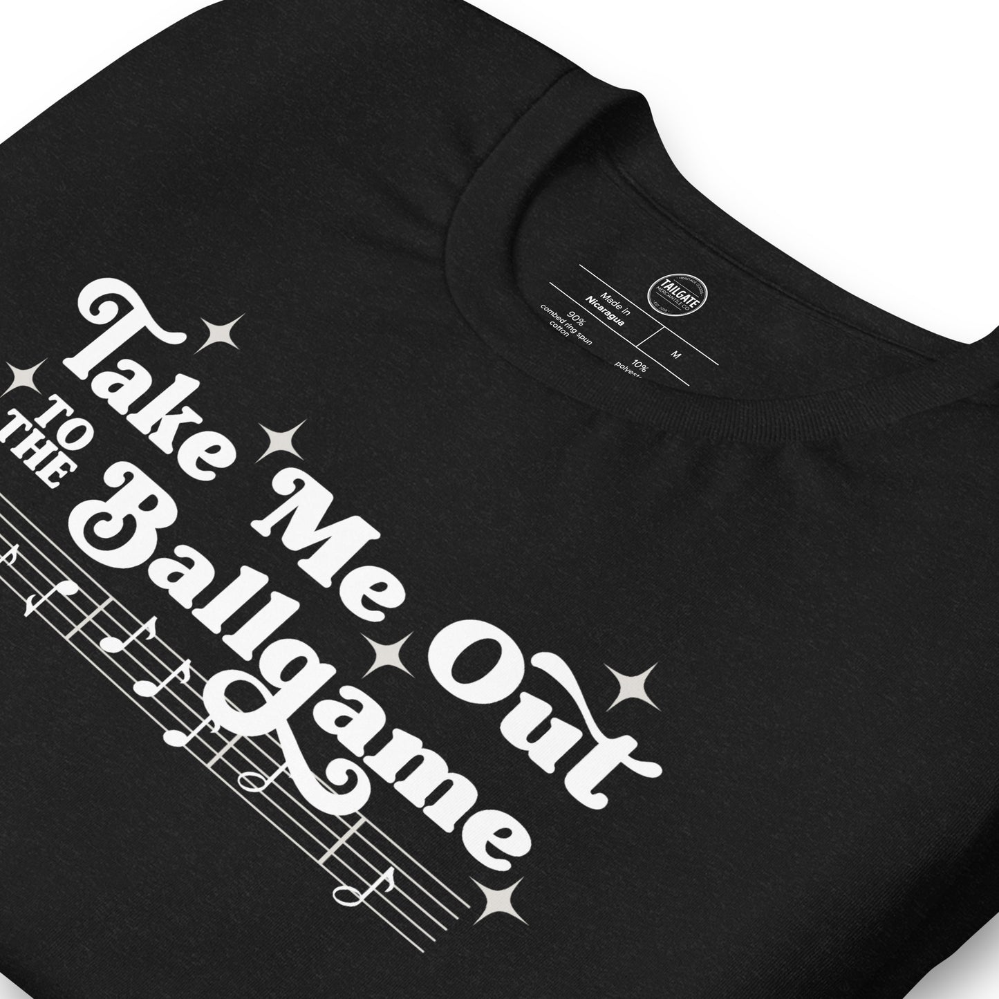 Close up image of heather black t-shirt with design of "Take Me Out to the Ballgame" with coordinating musical notes in white located on centre chest. This design is exclusive to Tailgate Mercantile and available only online.