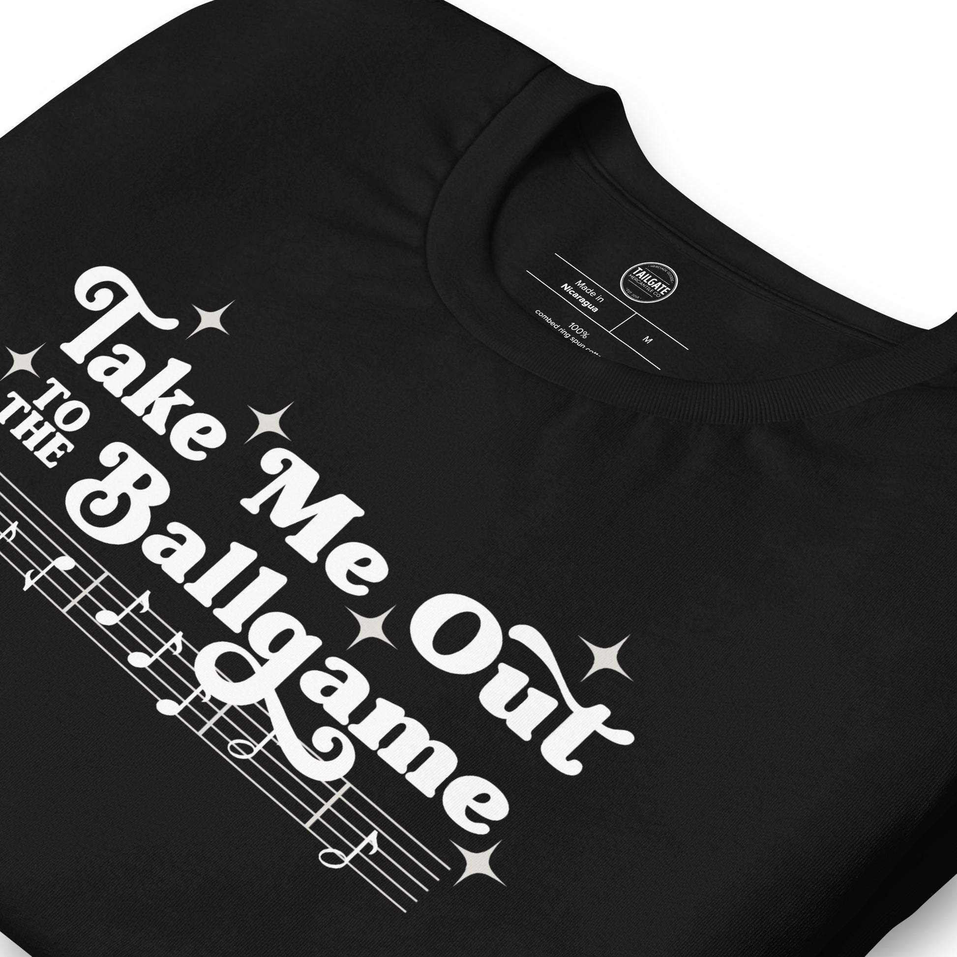 Close up image of black t-shirt with design of "Take Me Out to the Ballgame" with coordinating musical notes in white located on centre chest. This design is exclusive to Tailgate Mercantile and available only online.