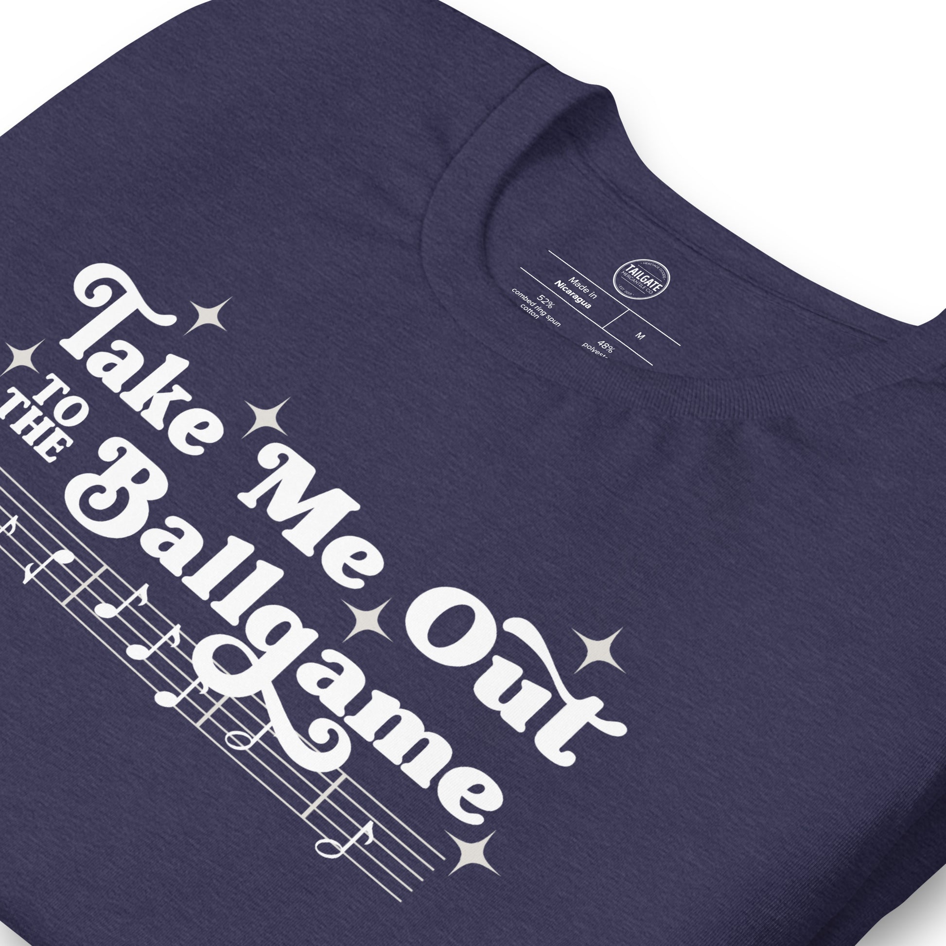 Close up image of heather navy t-shirt with design of "Take Me Out to the Ballgame" with coordinating musical notes in white located on centre chest. This design is exclusive to Tailgate Mercantile and available only online.