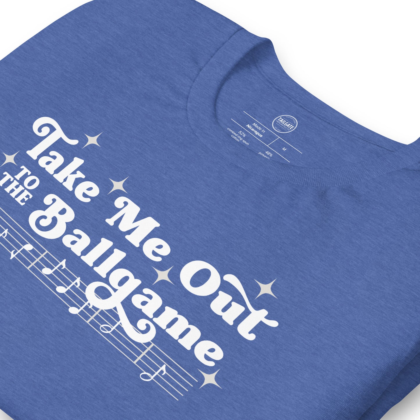Close up image of heather royal blue t-shirt with design of "Take Me Out to the Ballgame" with coordinating musical notes in white located on centre chest. This design is exclusive to Tailgate Mercantile and available only online.