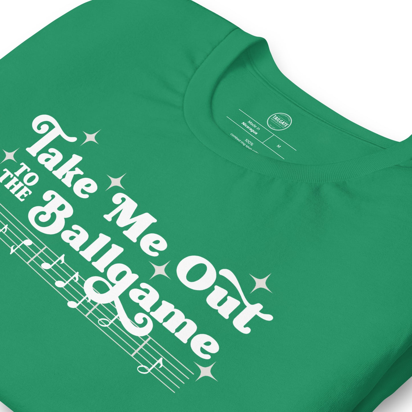 Close up image of kelly green t-shirt with design of "Take Me Out to the Ballgame" with coordinating musical notes in white located on centre chest. This design is exclusive to Tailgate Mercantile and available only online.