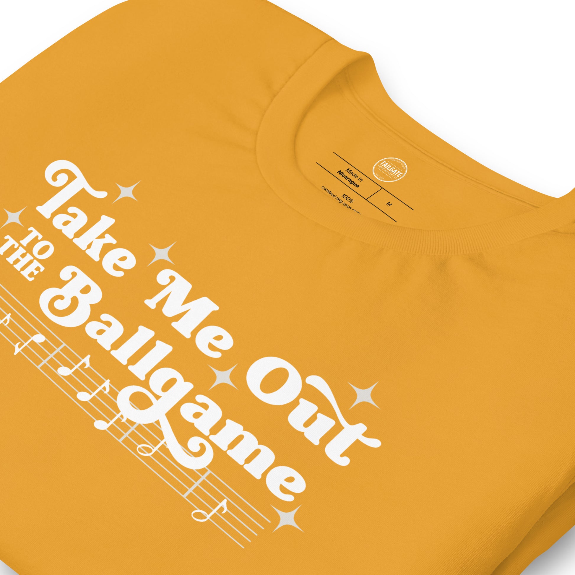 Close up image of mustard yellow t-shirt with design of "Take Me Out to the Ballgame" with coordinating musical notes in white located on centre chest. This design is exclusive to Tailgate Mercantile and available only online.