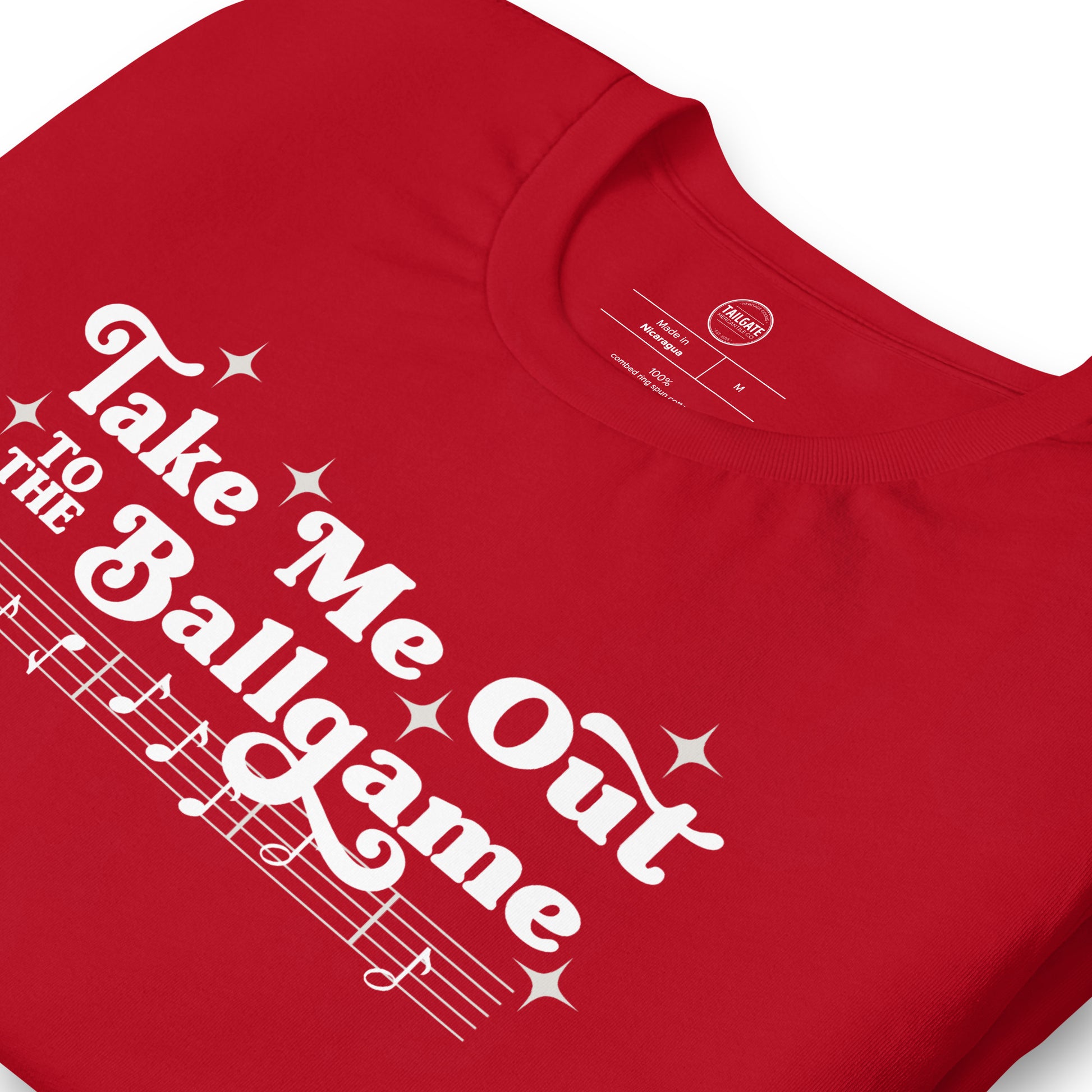 Close up image of red t-shirt with design of "Take Me Out to the Ballgame" with coordinating musical notes in white located on centre chest. This design is exclusive to Tailgate Mercantile and available only online.